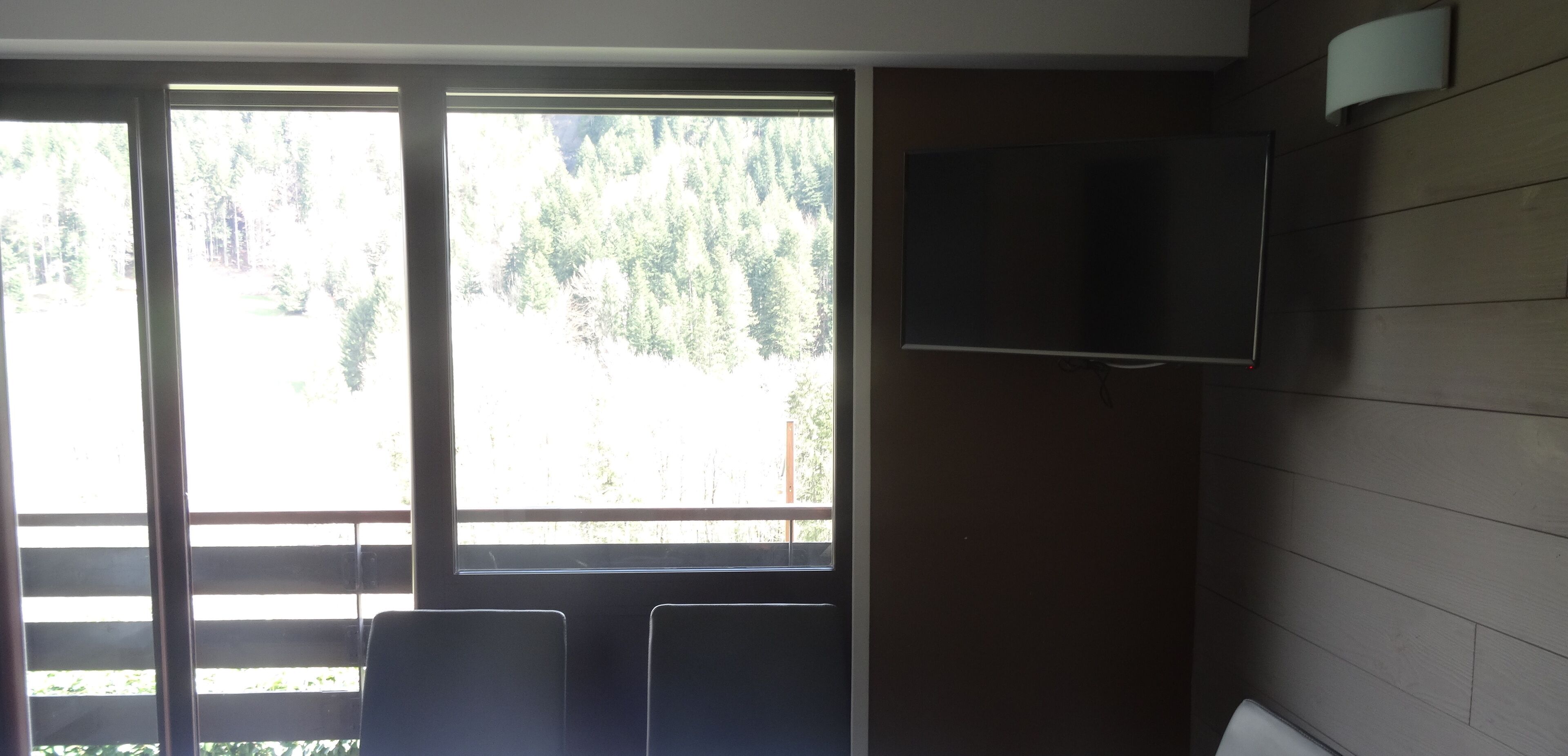 Une pièce dotée d’une grande fenêtre, d’un téléviseur à écran plat fixé au mur et de deux fauteuils.