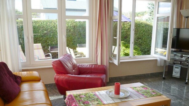 A living room with a red leather sofa, a yellow sofa, a wooden coffee table with a floral tablecloth, and a television on a stand.