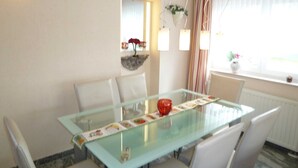 A dining area with a glass table, white chairs, a mirror, and a window with curtains.