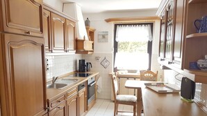 Une cuisine avec des meubles de rangement en bois, un évier, une cuisinière et un coin repas comprenant une table et des chaises.