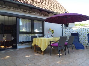 Une terrasse extérieure avec une table et des chaises, un parasol violet et un espace de jeux en arrière-plan.