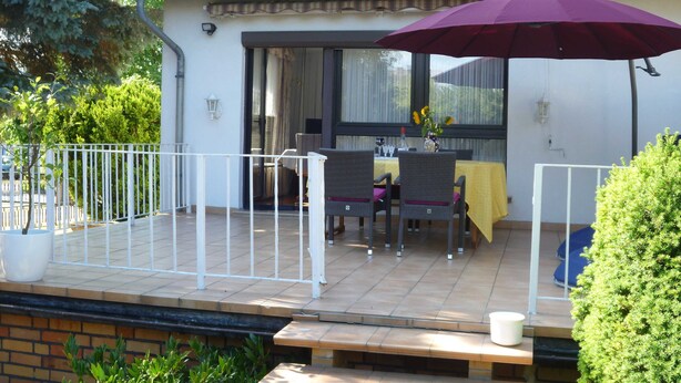 Une terrasse couverte avec une table et des chaises, un parasol violet et une balustrade blanche.