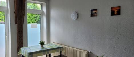 A room with a table, bench, two potted plants, a radiator, and artwork on the wall.