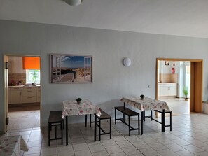Un coin repas avec deux tables, une cuisine à l’arrière-plan et un tableau représentant une scène de plage accroché au mur.