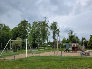 Ein Spielplatz mit Schaukeln, einer Kletterkonstruktion und einem umzäunten Bereich.