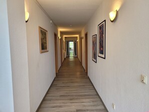 Un couloir d’hôtel avec un plancher en bois, des œuvres d’art encadrées accrochées aux murs et des luminaires fixés au mur.