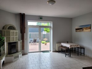 Ein Zimmer mit Kamin, einem Tisch mit floralem Tischtuch, einer Bank und einer Tür, die nach draußen führt.