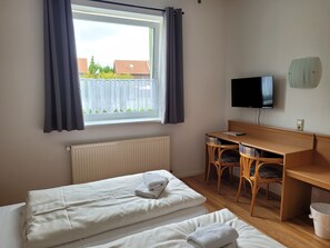 Ett rum med två sängar, ett skrivbord med stolar, en tv och ett fönster med gardiner.