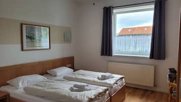 Un dormitorio con dos camas, una ventana con cortinas, un radiador, suelo de madera y un cuadro enmarcado en la pared.