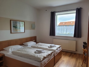 A bedroom with two beds, a window with curtains, a radiator, a wooden floor, and a framed picture on the wall. - DZ / 2-bed room 06_Ground floor - Guesthouse Am Schloss (Kramerhof)