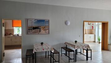 Een eetruimte met twee tafels, een keuken op de achtergrond en een schilderij van een strand.