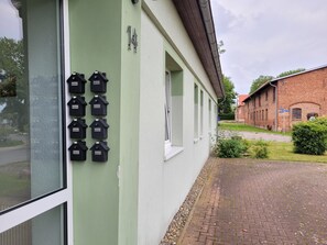 A building with a green facade, a row of black mailbox-like objects, and a brick building in the background.