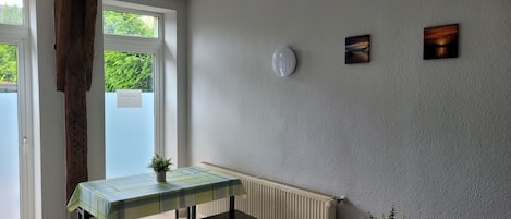 Una habitación con una mesa, un banco, dos plantas en macetas, un radiador y obras de arte en la pared.