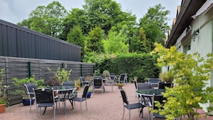 A patio area with tables and chairs, surrounded by potted plants and a brick floor. - DZ / 2-bed room 06_Ground floor - Guesthouse Am Schloss (Kramerhof)
