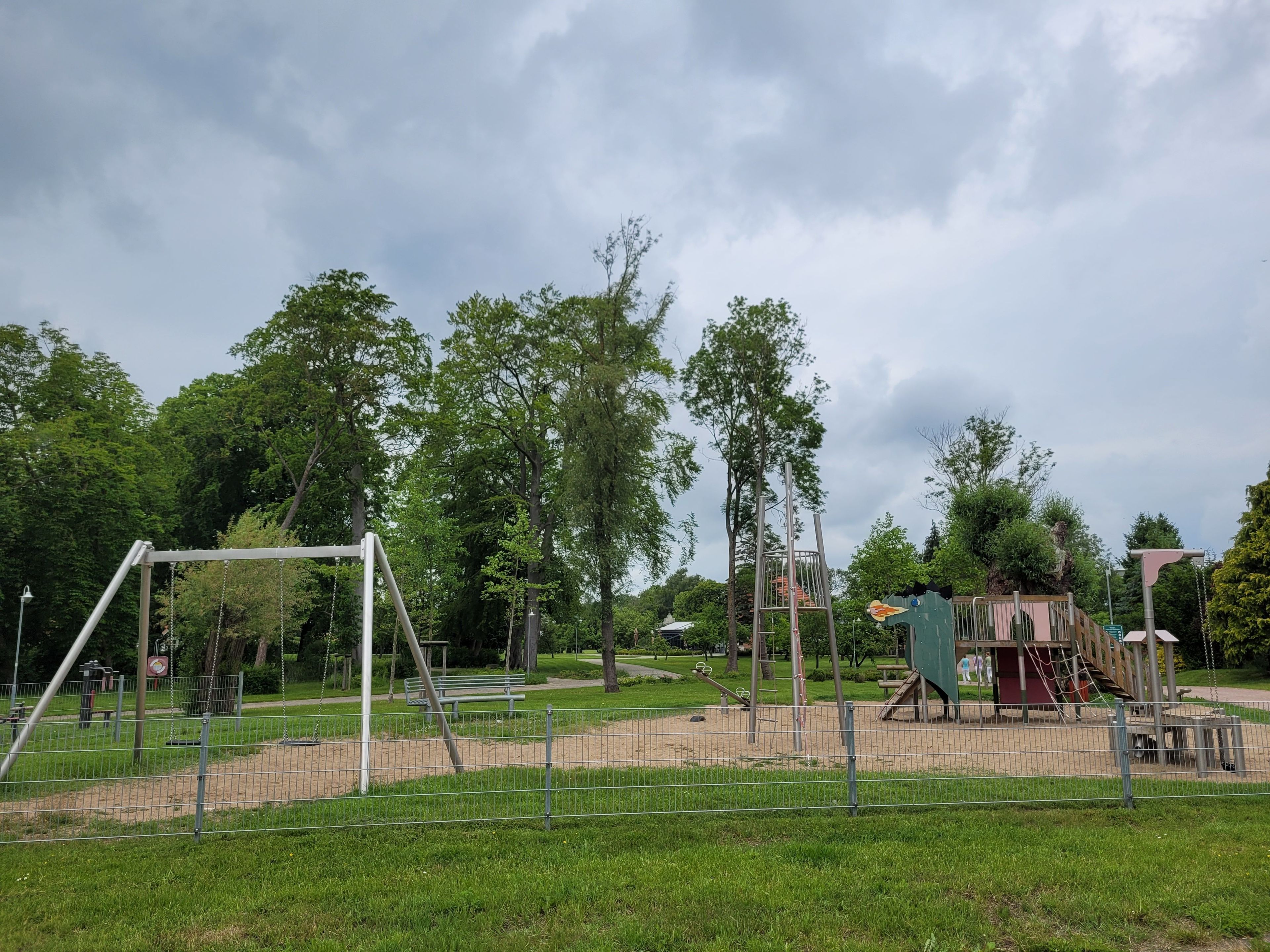 Ein Spielplatz mit Schaukeln, einer Kletterkonstruktion und einem umzäunten Bereich.
