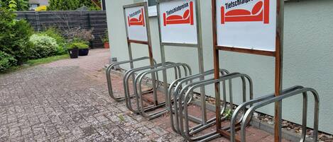 A row of metal-framed beds with signs indicating 'Tiefschlafpreise' (deep sleep prices) in a courtyard with a paved walkway.