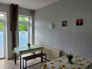 Ein Zimmer mit Tisch, Bank, zwei Blumentöpfen, einer Heizung und Bildern an der Wand.
