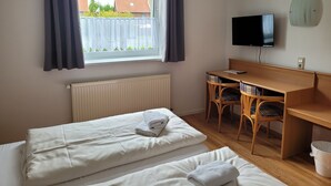 Ein Zimmer mit zwei Betten, einem Schreibtisch mit Stühlen, einem Fernseher und einem Fenster mit Vorhängen.