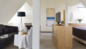 Una habitación de hotel moderna con un sofá, un escritorio con computadora, una cama y un televisor.