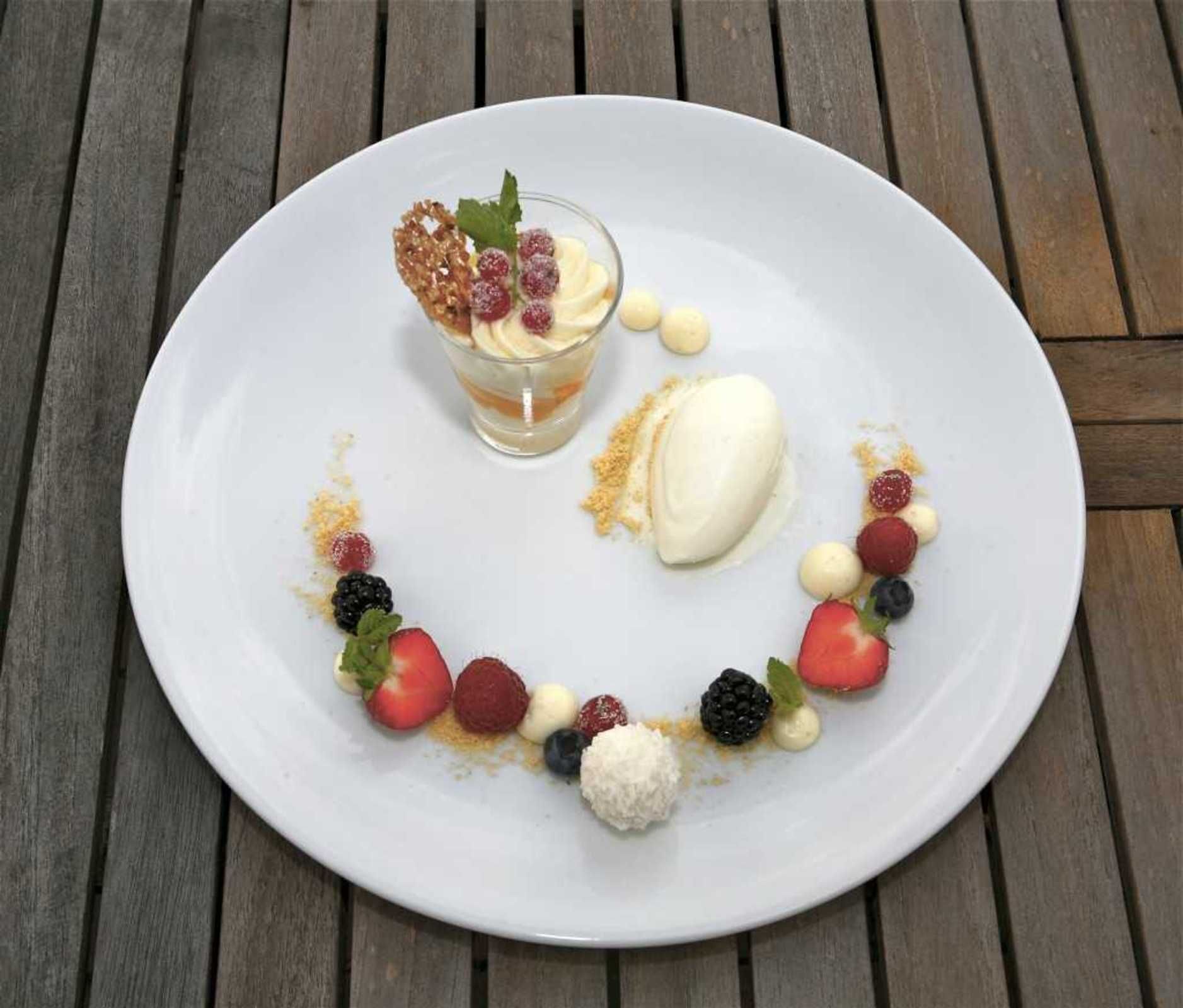 Une assiette de dessert avec divers fruits et un petit récipient en verre sur une table en bois.