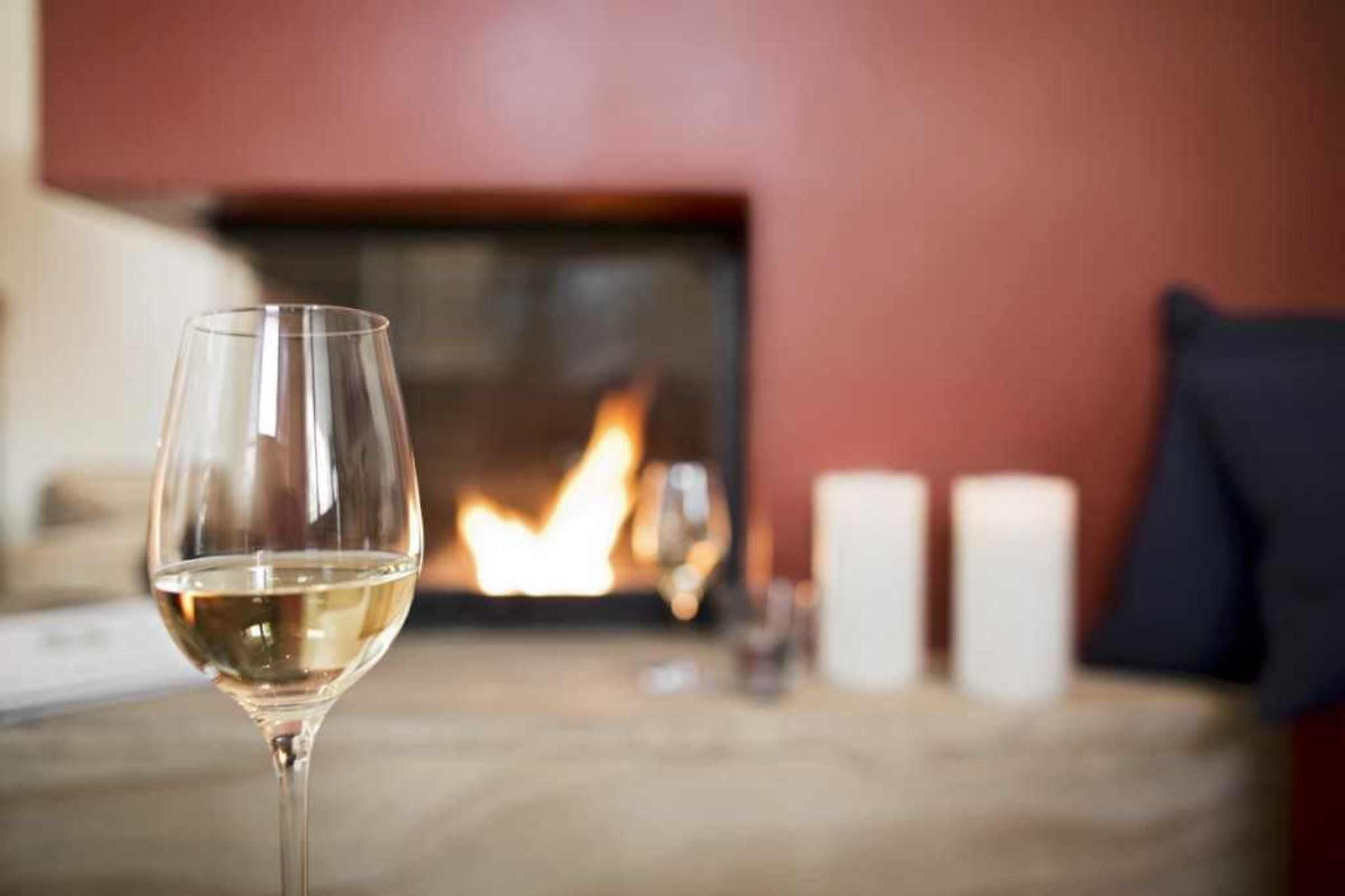 A glass of white wine on a table with a fireplace in the background.