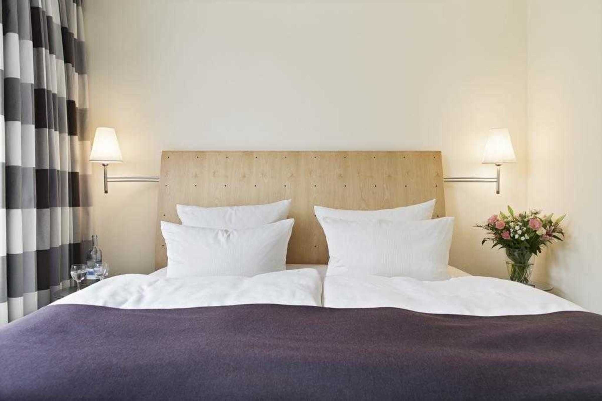 Ein Hotelzimmer mit einem großen Bett, zwei Nachttischlampen, einem Holz-Kopfteil und einer Vase mit Blumen.