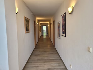Ein Hotelgang mit Holzboden, gerahmten Kunstwerken an den Wänden und Wandleuchten.