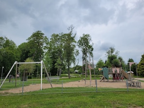 Un parque infantil con columpios, una estructura para escalar y una zona vallada.