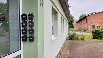 A building with a green facade, a row of black mailbox-like objects, and a brick building in the background.