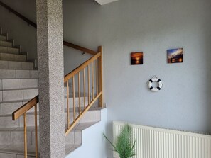 Una escalera con barandillas de madera, un muro con textura y dos cuadros enmarcados.