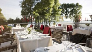 An outdoor dining area with tables set for two, surrounded by trees and a railing. - Seaside snuggle room - Hotel Kleines Meer Object ID 129080 (Waren (Müritz))