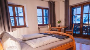 Una habitación acogedora con una cama de madera, una mesita con una planta y ventanas grandes con cortinas.