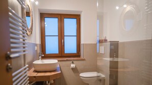 Un baño moderno con tocador de madera, lavamanos independiente, inodoro y zona de ducha con mampara de vidrio.