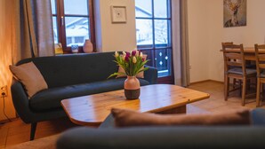 Una sala de estar acogedora con un sofá, una mesa de centro con un jarrón de flores, una mesa de comedor con sillas y un cuadro en la pared.