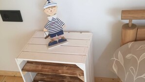 Ein kleiner Nachttisch aus Holz mit Ablagefläche, ein hölzernes Bettgestell und ein Bett mit floralem Überwurf.