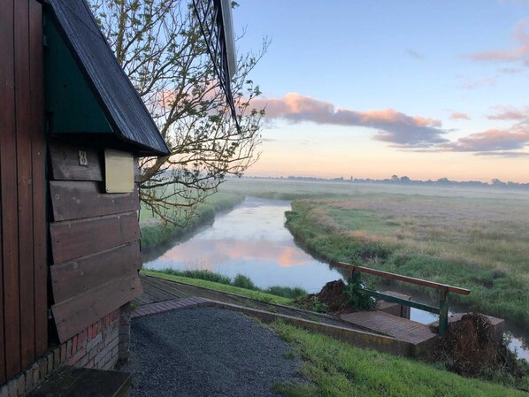 A wooden cabin with a view of a river and open fields.