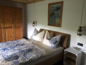 A bedroom with a bed, pillows, a hanging lantern, a painting, and a wooden wardrobe.