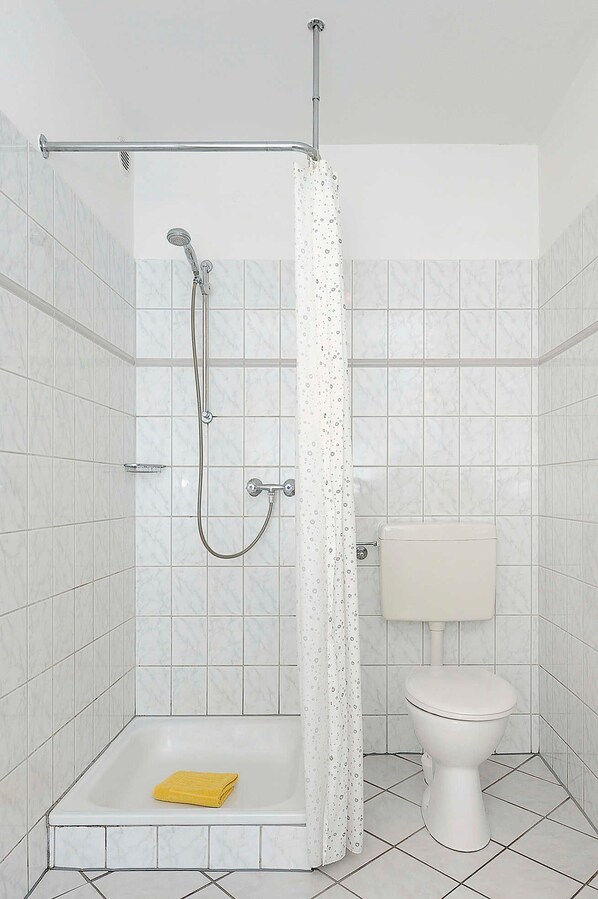 A shower with a glass door, a yellow bath mat, and a toilet with a white tank.