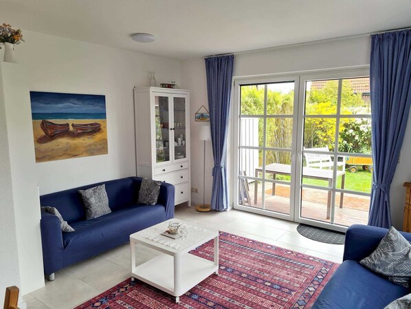 Un salon avec un canapé bleu, une table basse blanche et un tapis à motifs. On y trouve une vitrine et un tableau accroché au mur.