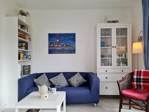 Un salon avec un canapé bleu, un meuble blanc, une bibliothèque et un tableau représentant un phare.
