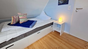 Un dormitorio pequeño y acogedor con una cama individual, una mesita de noche con lámpara, una puerta y un cuadro colgado en la pared.