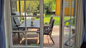Un invernadero con zona de patio que incluye una mesa, sillas, un jardín pequeño y una valla de madera.