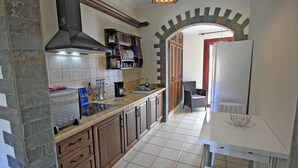 Eine Küche mit Steinwänden, Holzschränken, einer gefliesten Spritzschutzwand und einem weißen Tisch mit einem Korb.