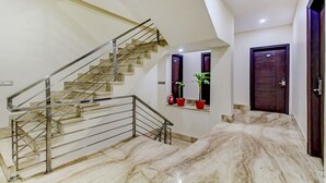 Un escalier moderne avec des rampes en métal, un sol en marbre et une plante en pot sur la plateforme.