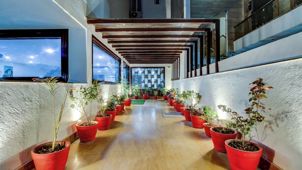 Un couloir orné de plantes en pot aux feuilles rouges, avec des poutres en bois et une vue sur la ville grâce à de grandes fenêtres.