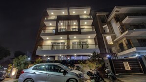 Un immeuble à plusieurs étages doté de balcons, avec une voiture et des motos garées devant.