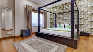 Un lit à baldaquin avec vue sur la ville par la fenêtre, un petit bureau avec un téléphone et un mur décoratif orné d’un motif.