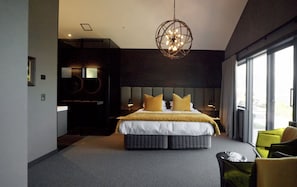 A modern hotel room with a large bed, a television, a seating area, and a view through the window.