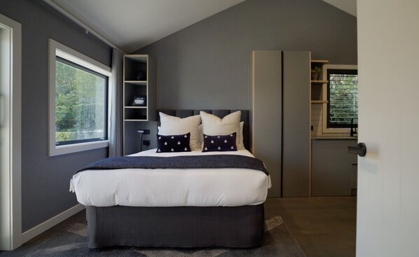 Ein modernes Schlafzimmer mit einem großen Bett, Einbauschränken und Blick durch ein Fenster.