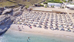 Oversigtsbillede af en strand med mange liggestole og parasoller, en klippekyst og nogle bygninger i baggrunden.
